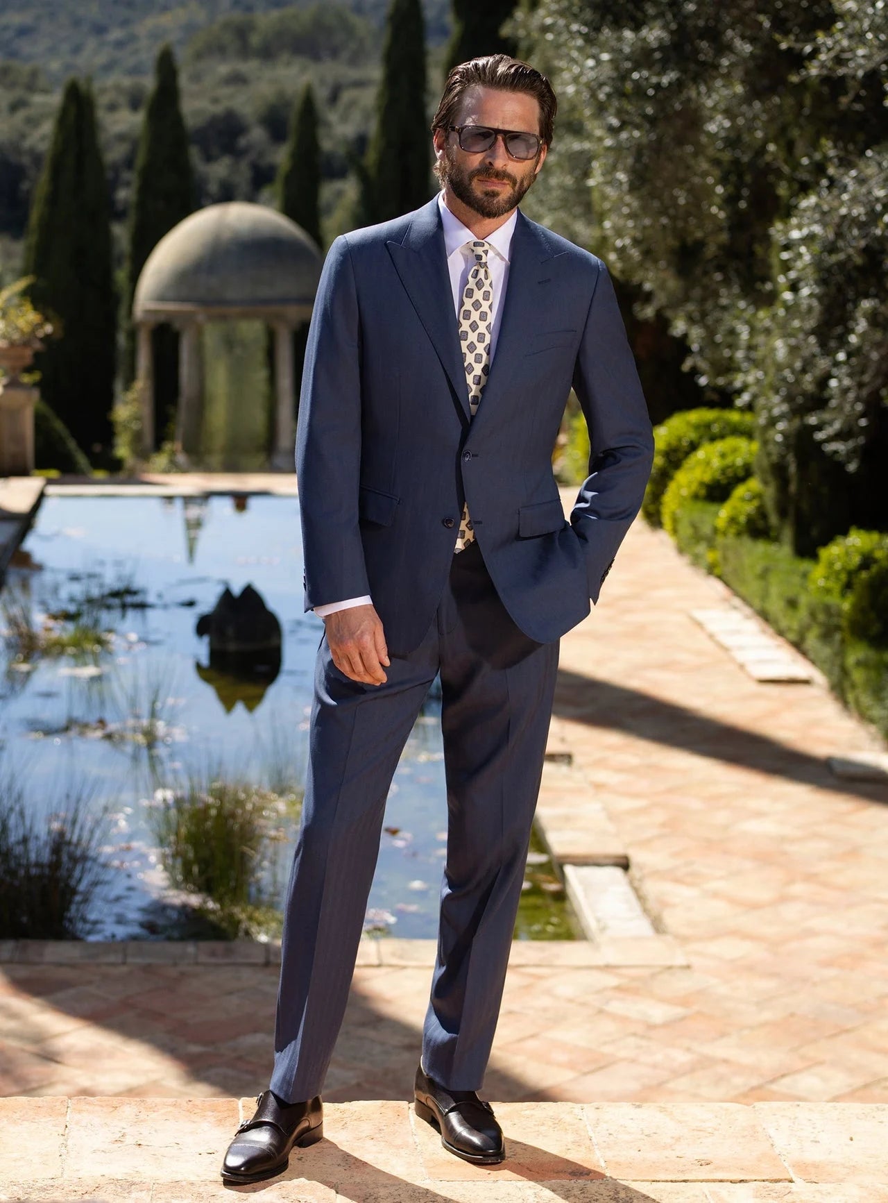 A navy Consiglieri men's suit, with a white shirt and tie, in the garden